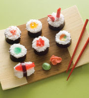 Faux sushi on a wooden platter with chopsticks beside them.