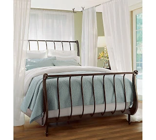 A very light blue and white blanket on a metal bed frame.