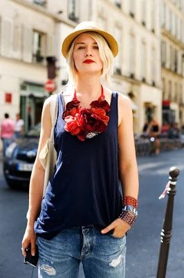 A red floral necklace on a woman wearing a blue shirt.