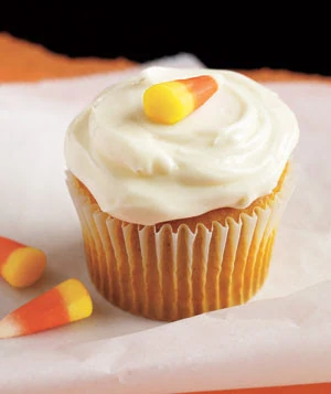 A pumpkin cupcake with cream cheese frosting with candy corn on top and beside it.