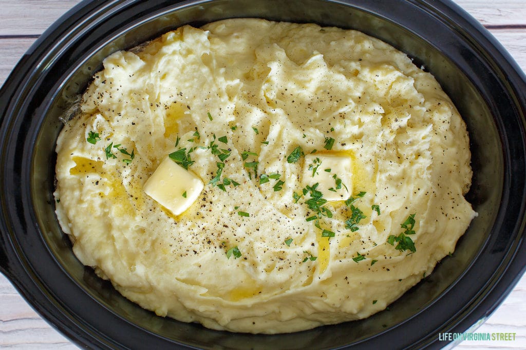 The crock pot filled with mashed potatoes and butter on the top.