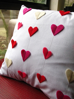 A white pillow with red, pink and cream hearts all over it.