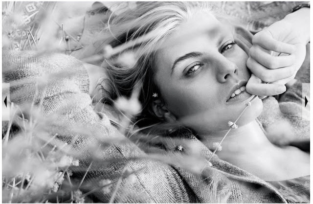A model lying on the ground with a piece of grass in her hand.
