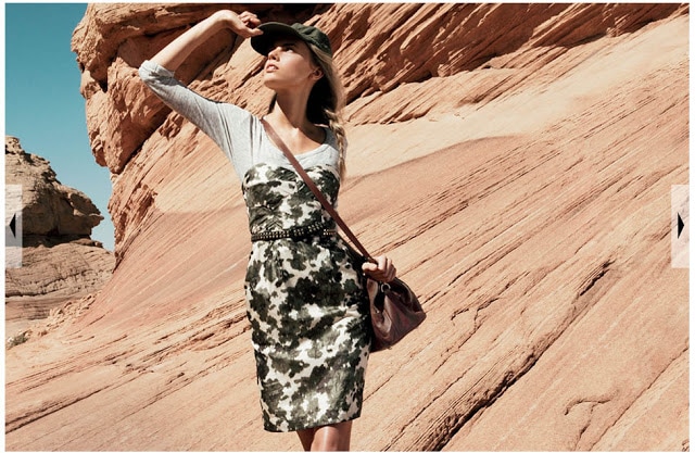 A dress overtop a long sleeved shirt with a belt and a purse slung over one shoulder looking in the sky.