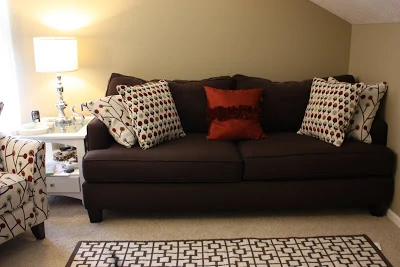 A dark brown couch with pillows on it and a small area rug in front of the couch.