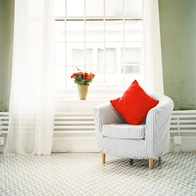 A herringbone white rug with a striped armchair and a red pillow.
