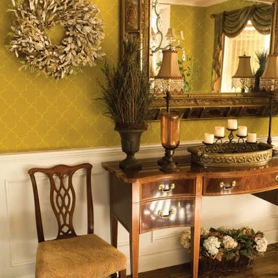 A mustard coloured stencilled wall with a wooden side table and a wreath on the wall.