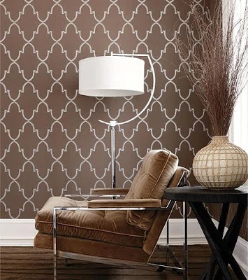 A brown chair, a lamp and side table beside a wall that has a pattern on it in brown and white.
