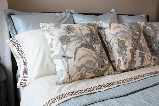 A light blue bedspread with floral pillows in blue and gold.