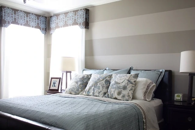 The master bedroom with a striped wall and a large bed near the corner window.