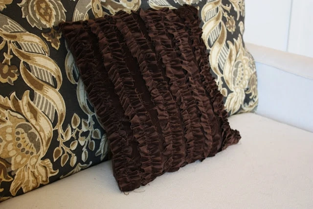 Brown velvet ruffled pillow on couch.