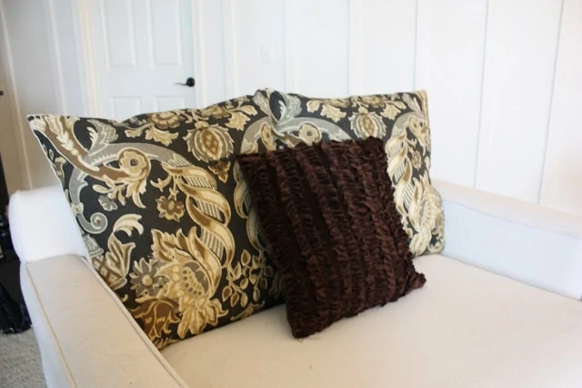 Ruffled velvet pillow on chair with two other patterned pillows.