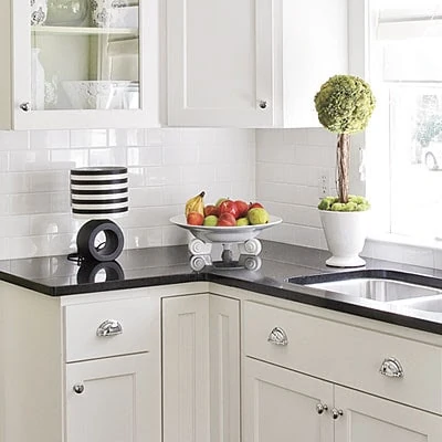 A white kitchen with a black countertop and a topiary on the counter.