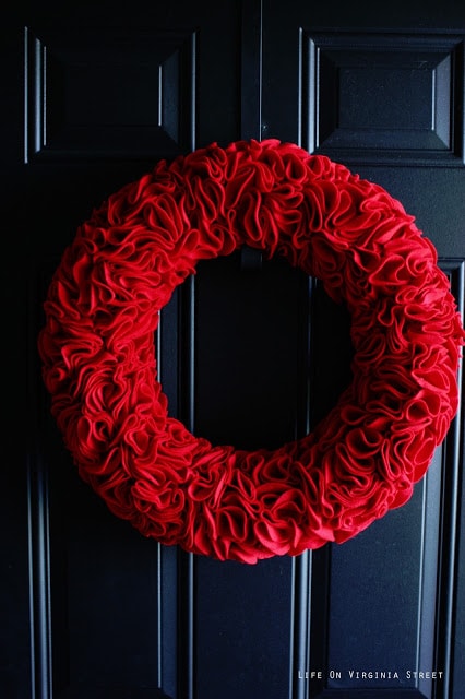 Up close view of the red ruffles on the wreath hanging on the dark door.