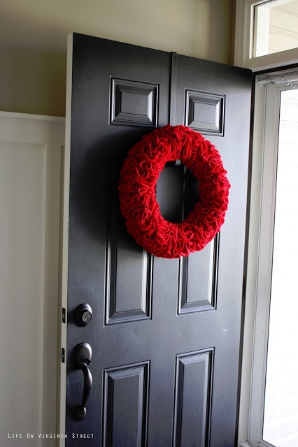 An opened door with the red ruffle wreath hanging on it.