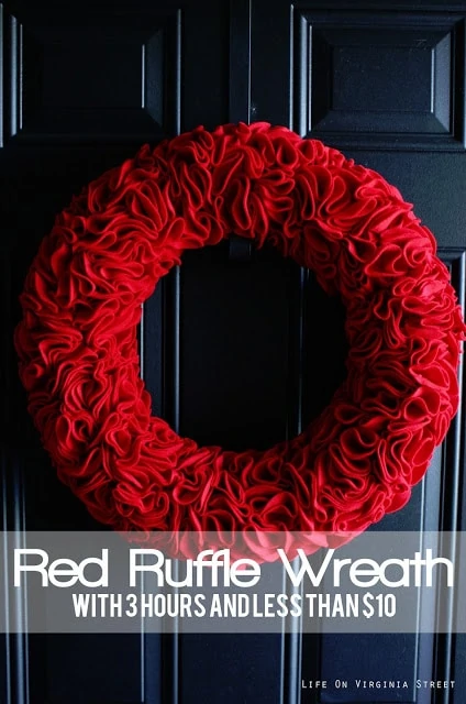 A darling red ruffle wreath made with felt and stick pins hanging on a dark wood door.