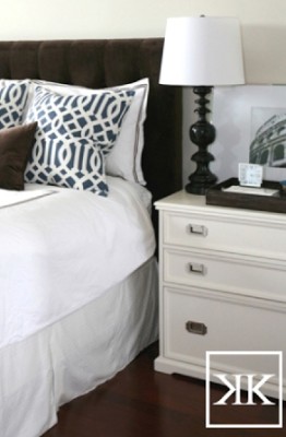 A brown headboard with white sheets and blue pillows.