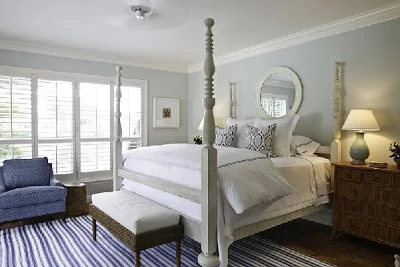 A white four poster bed with a blue and striped rug by it.