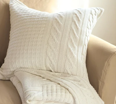 A white neutral sweater pillow on the chair.