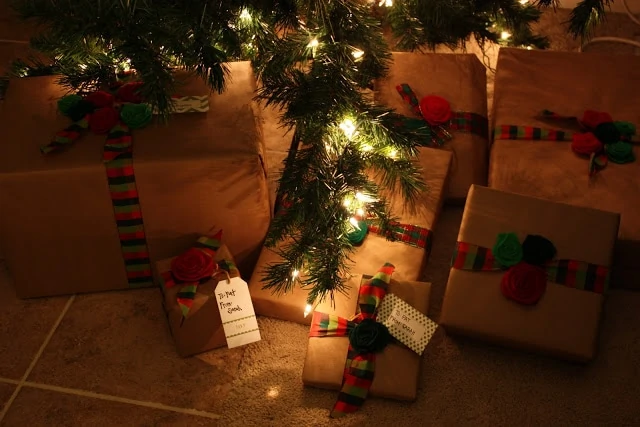 Many presents under the Christmas tree which is illuminated by lights.