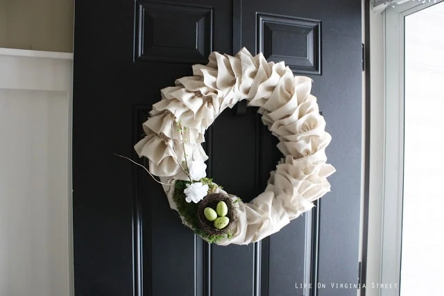 A white wreath hanging on a black door and the door is open.