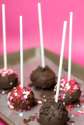Chocolate cake pops on sheet with sprinkles on it.