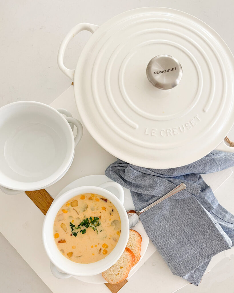 The best turkey corn chowder in a white soup bowl, shown with a white Dutch oven, wood serving board, and blue napkin.