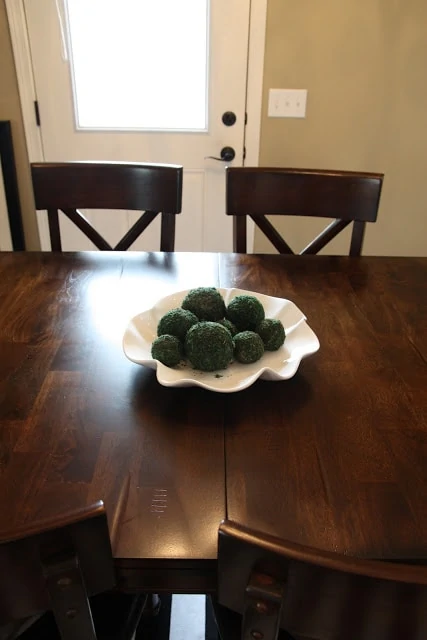 Wooden dining room table with a white bowl filled with greenery in the middle of it.