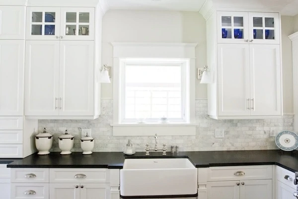 Carrera Marble tile, a farmhouse sink, and white cabinets in the kitchen.