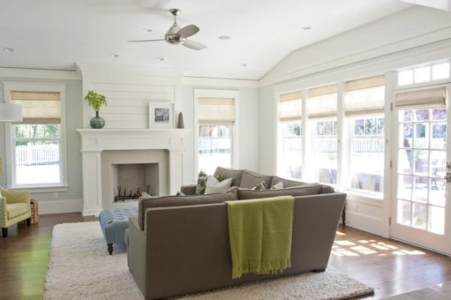 A neutral painted living room with a light brown couch and green blanket on the back of the couch.