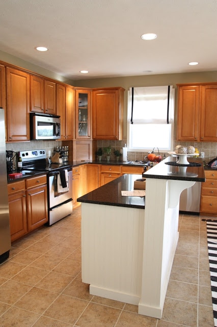 A kitchen with light brown wood cabinets and a white half island with dark countertop.