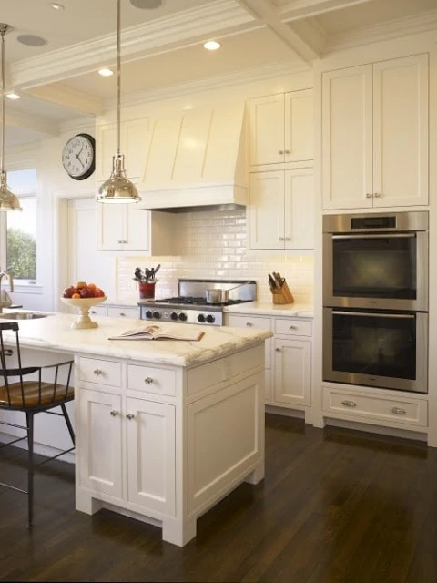 A white kitchen with hardwood floor, and pendant lamp above the island.