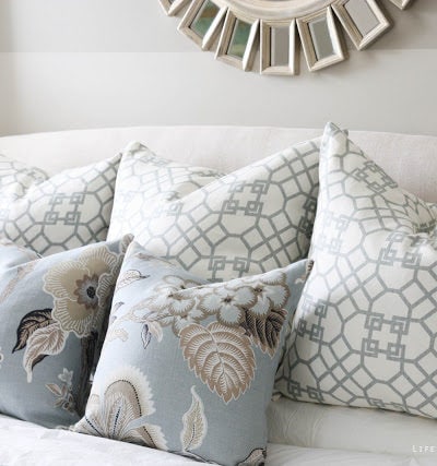 Bedroom with striped walls, white bedding, blue and gray pillows, sunburst mirror and chandelier.