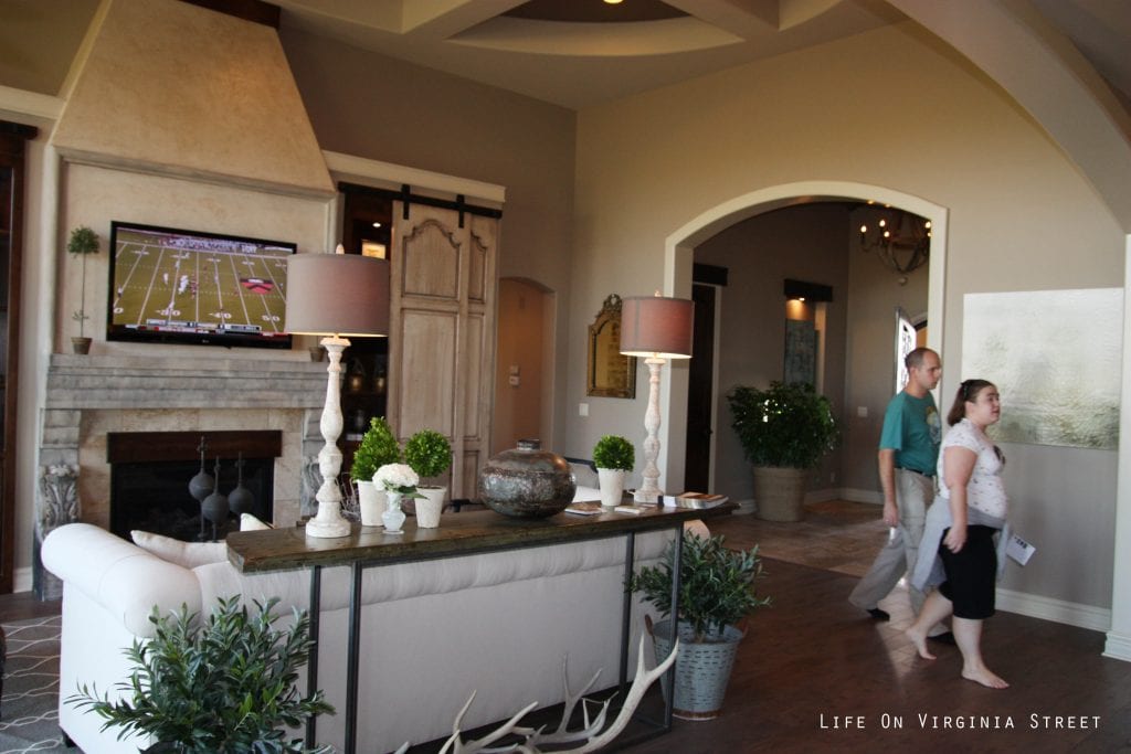  Linen chesterfield sofa, built-in entertainment center with wood shutters, boxwood plants, iron and wood table, hardwood floors.