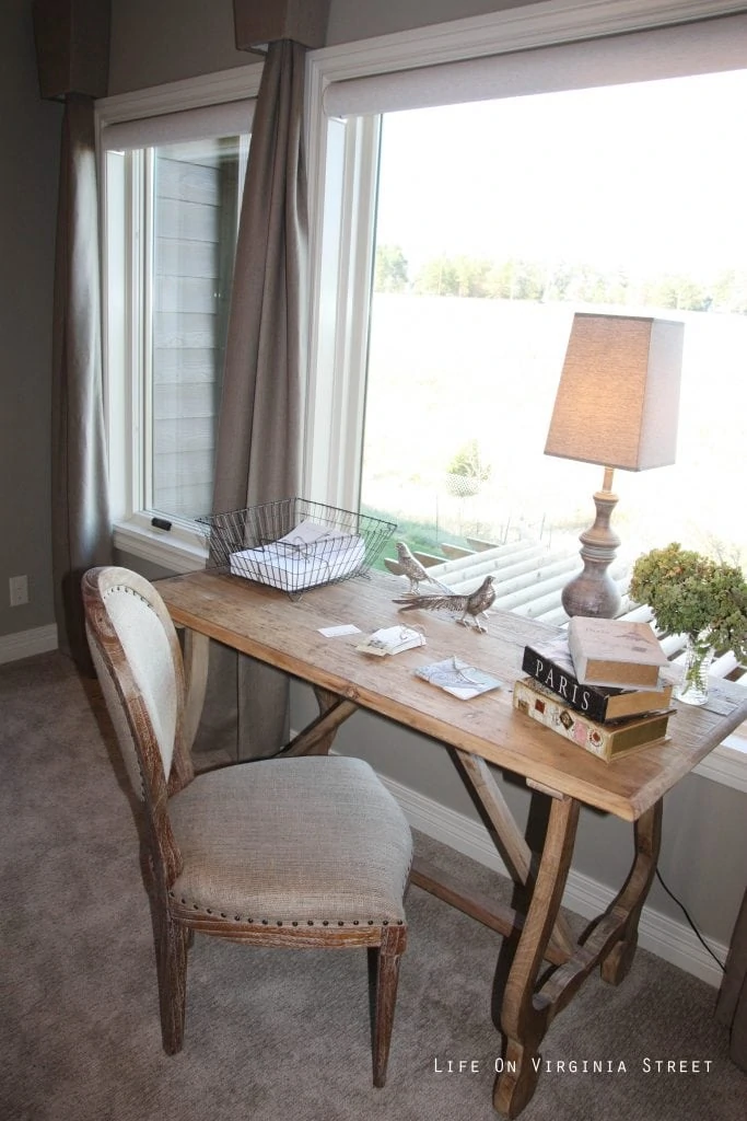 Writing nook in master bedroom with French-style desk and linen chair.