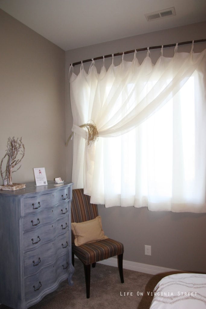 A white curtain hanging in the bedroom tied to the side.