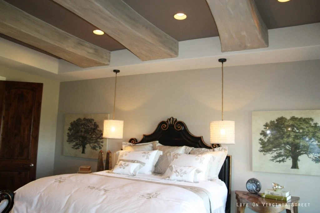 Master bedroom with faux wood beams on ceiling and hanging pendant lights over nightstand.