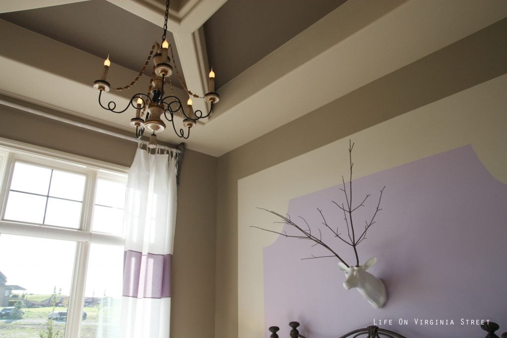 Girls bedroom with tan walls and lavender accents. Faux deer head with stick antlers and French chandelier.