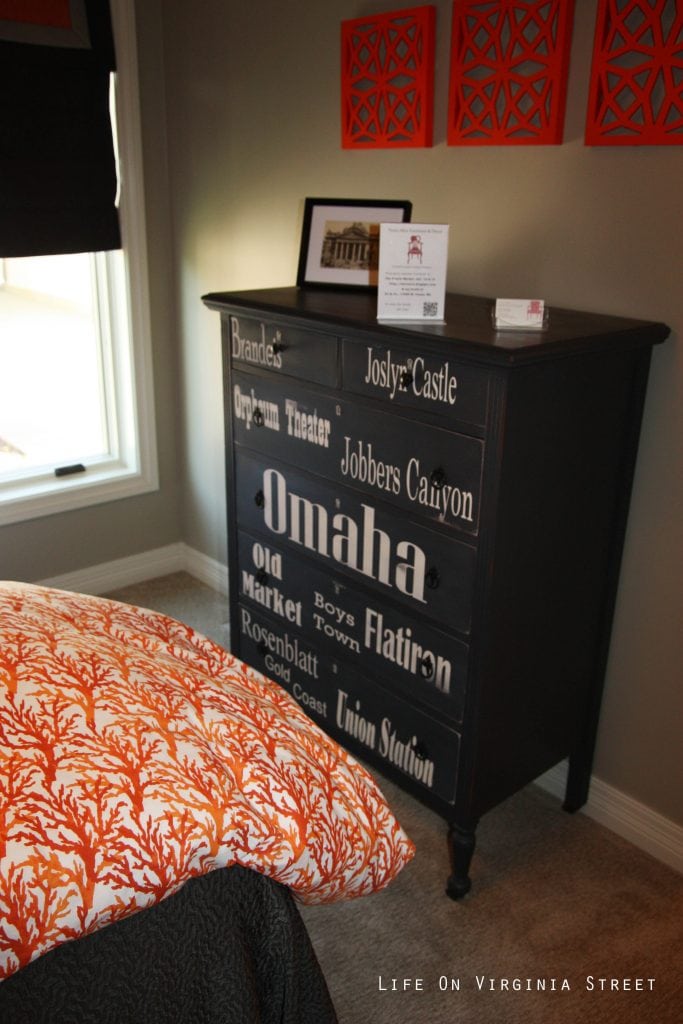 Black and white dresser with Omaha landmarks in a orange coral and navy blue bedroom.