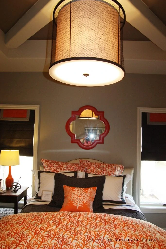 A large chandelier over a bed with orange bedspread and a red mirror.