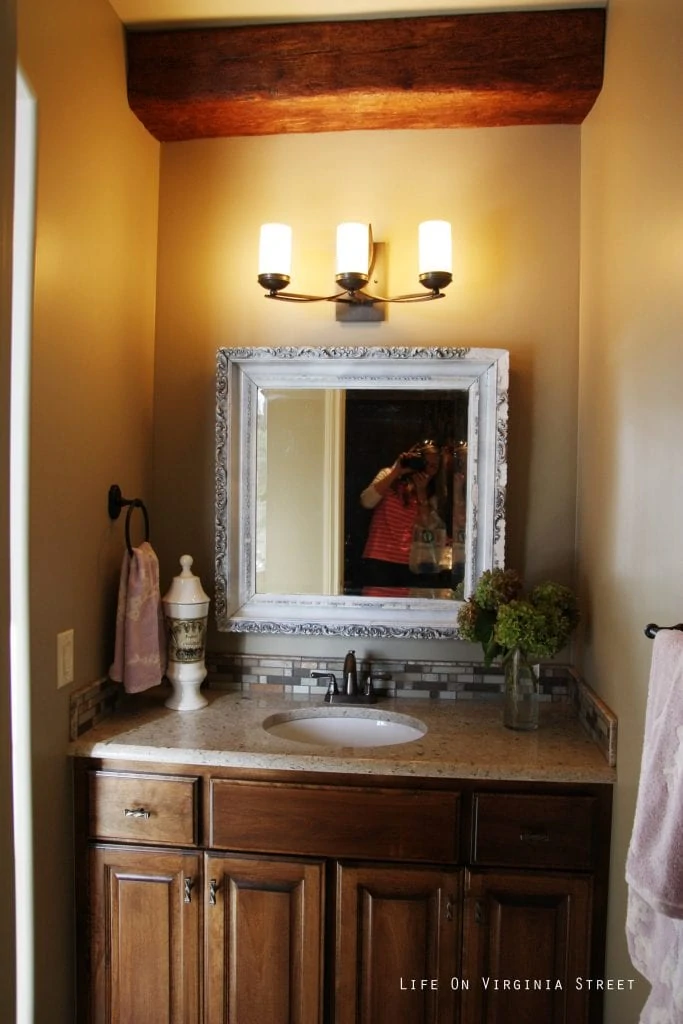 A vanity in the bathroom with a white ornate mirror and wooden beam.