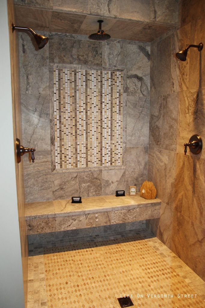 A walk in shower with three shower heads and a shower bench.