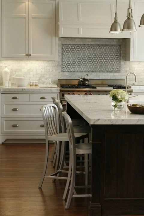 Kitchen island with a marble top and pendant lights over top of it.