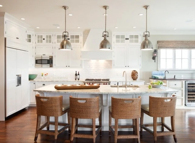 Four wicker chairs in front of a white kitchen island with three lights above it.