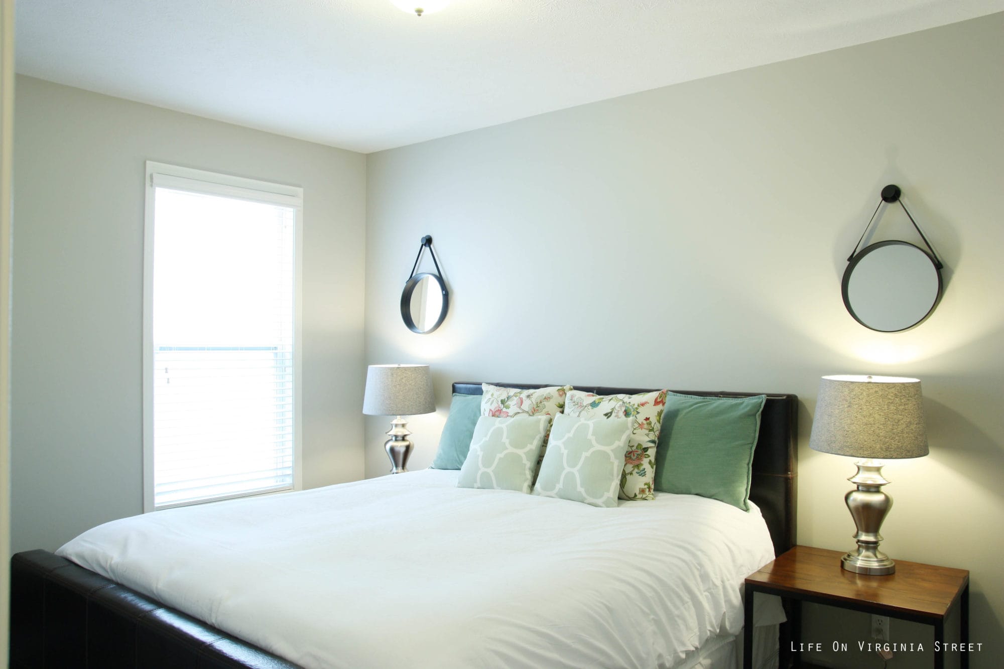 A neutral bedroom with small lamps on a side table beside the bed.