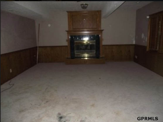 A black and gold fireplace with wood around it and old carpet.