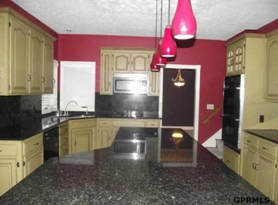 A kitchen with off white cabinets, black granite, and red accents.