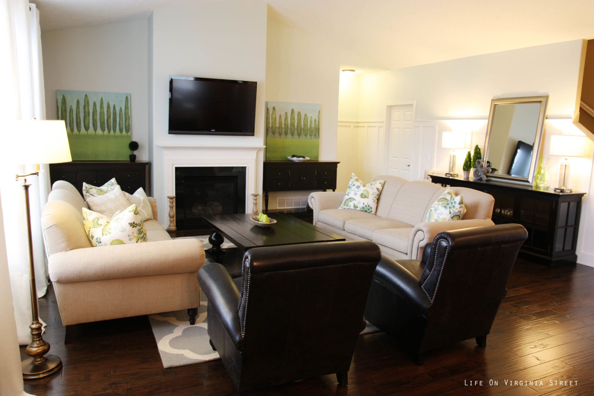 The living room with a white fireplace, leather chairs and neutral couches.