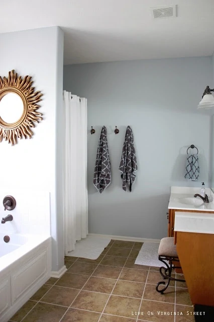 The master bathroom with a gold round sunburst mirror above the tub, and towels hanging on hooks in the bathroom.