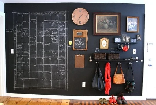 Large chalkboard wall with clock, pictures and hooks on it.